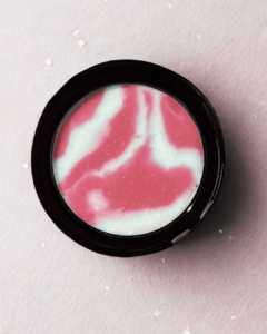 Open compact of Genuist Beauty’s Smooth Reflection light-diffusing face primer showing pink and white marbled formula on a soft pink background.